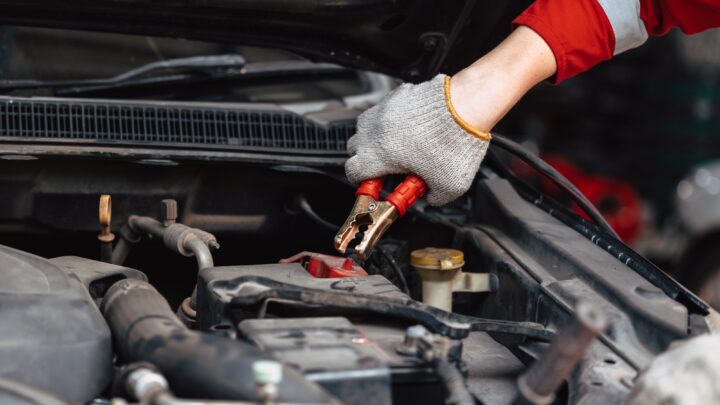 closeup mechanic male hand holding battery clamps grip for charging car battery in auto repair works