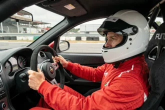 Pilote en combinaison rouge au volant d'une voiture de circuit lors d'un stage de pilotage
